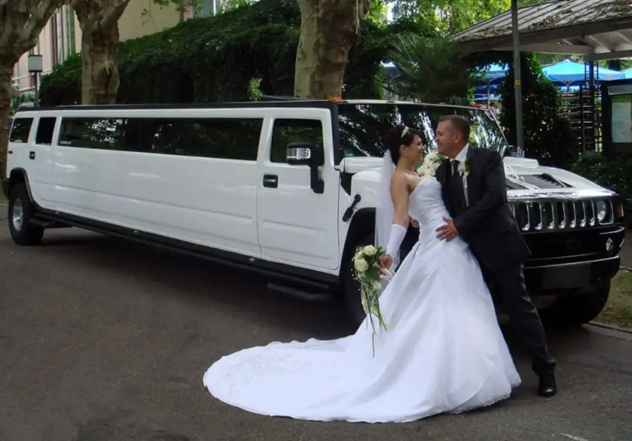 Imagen de novios besándose detrás sale una limusina Hummer