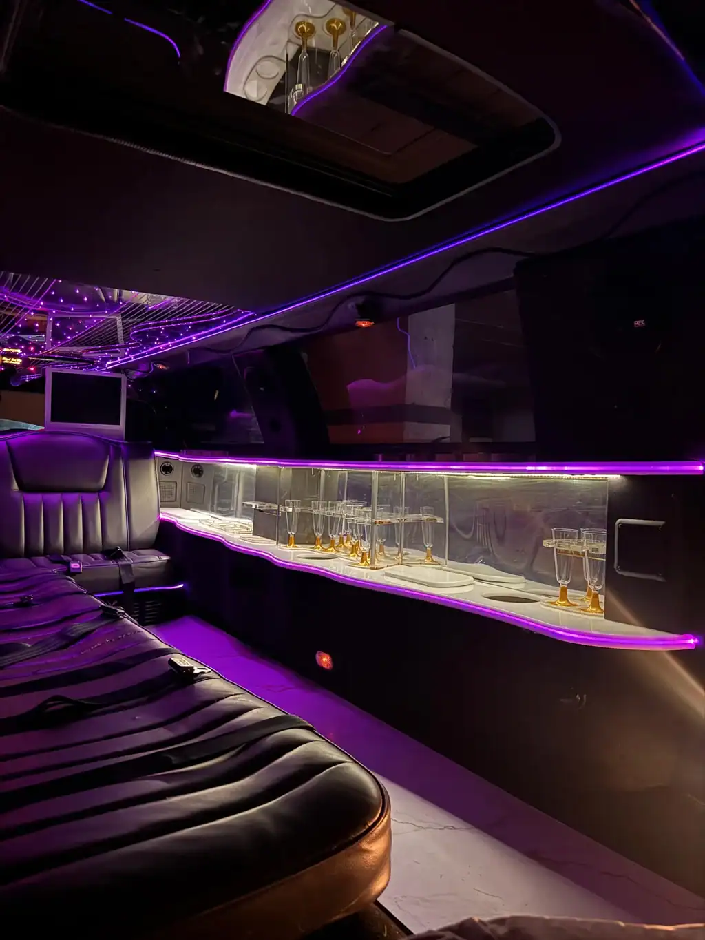 Detalle del interior color lila de una limusina Lincoln blanca, mostrando la barra con botellas y copas de cristal, perfecta para celebraciones en Barcelona