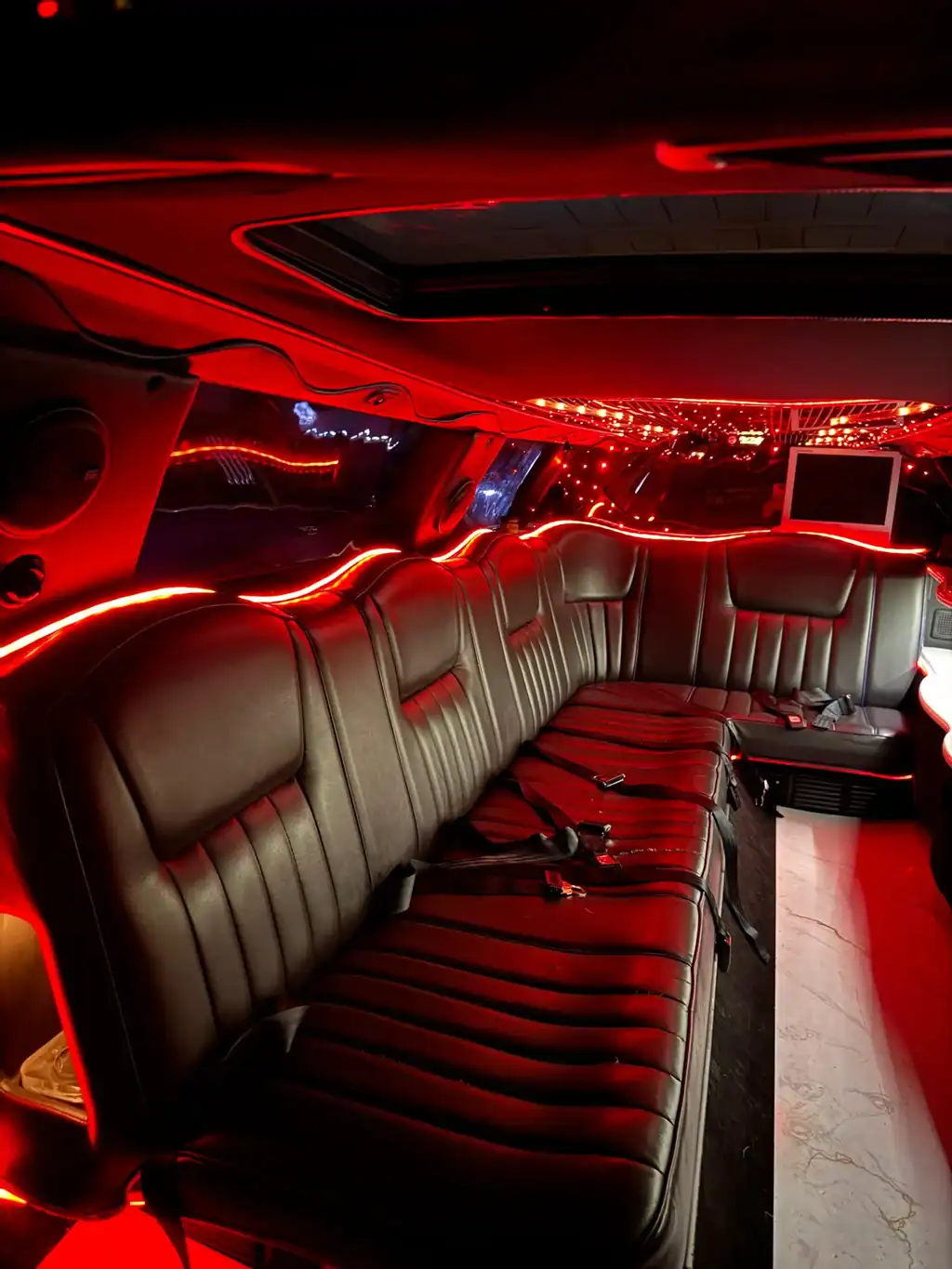 Barra interior iluminada en tonos lila y rojo de una limusina Lincoln blanca, con copas y botellas listas para eventos exclusivos en Barcelona