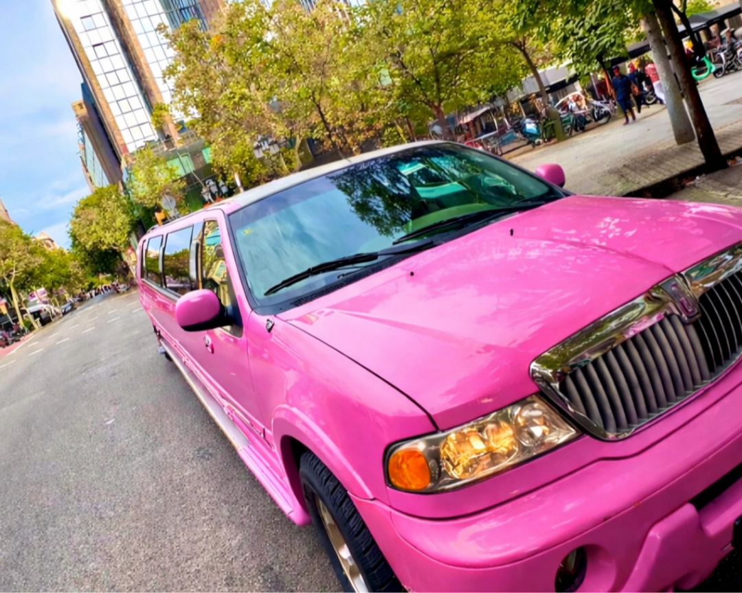 Limusinas-Rosas Frontal de limusina Hummer rosa Barbie en carretera de Barcelona con edificios emblemáticos, alquiler limusina premium